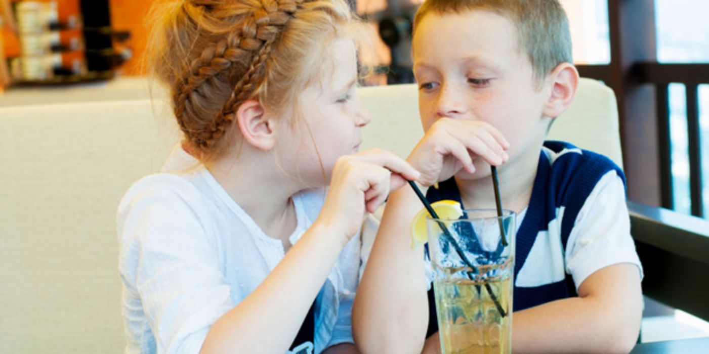 Mädchen und Junge, ca. 6 Jahre, trinken am Tisch gemeinsam aus Limoglas mit Strohhalm