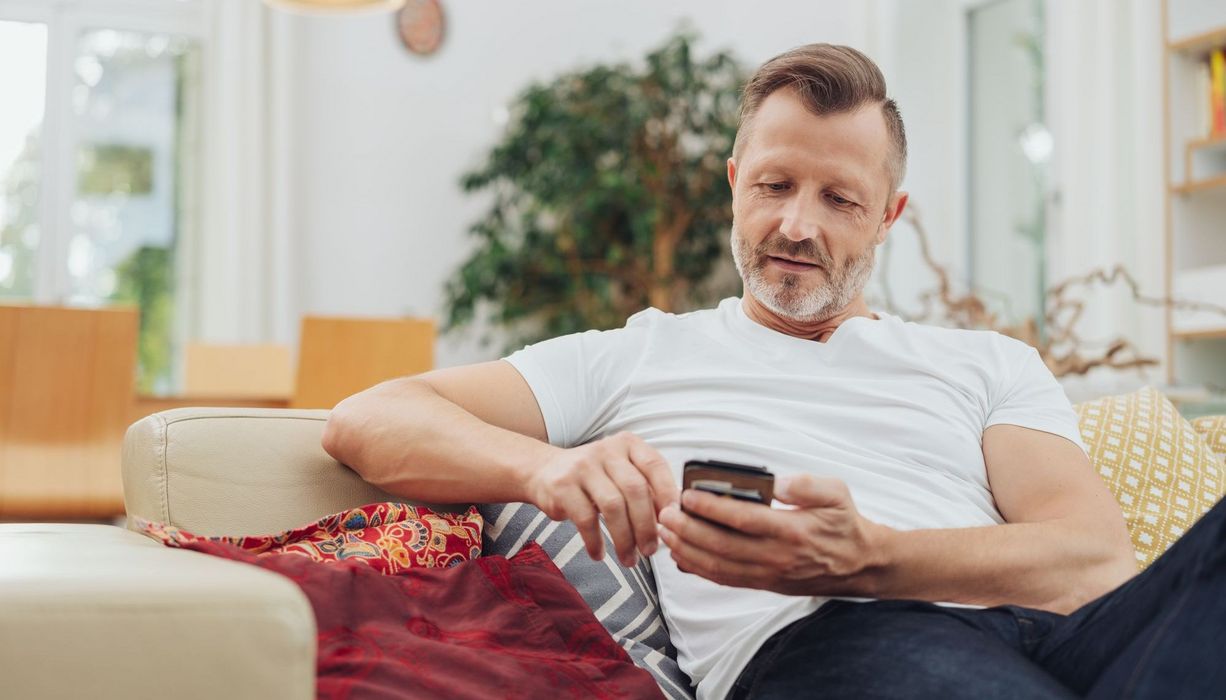 Älterer Mann, mit Smartphone auf der Couch.