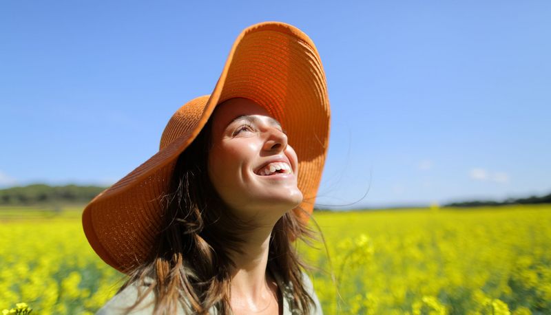 Junge Frau mit Sonnenhut, lächelt und schaut in den Himmel.