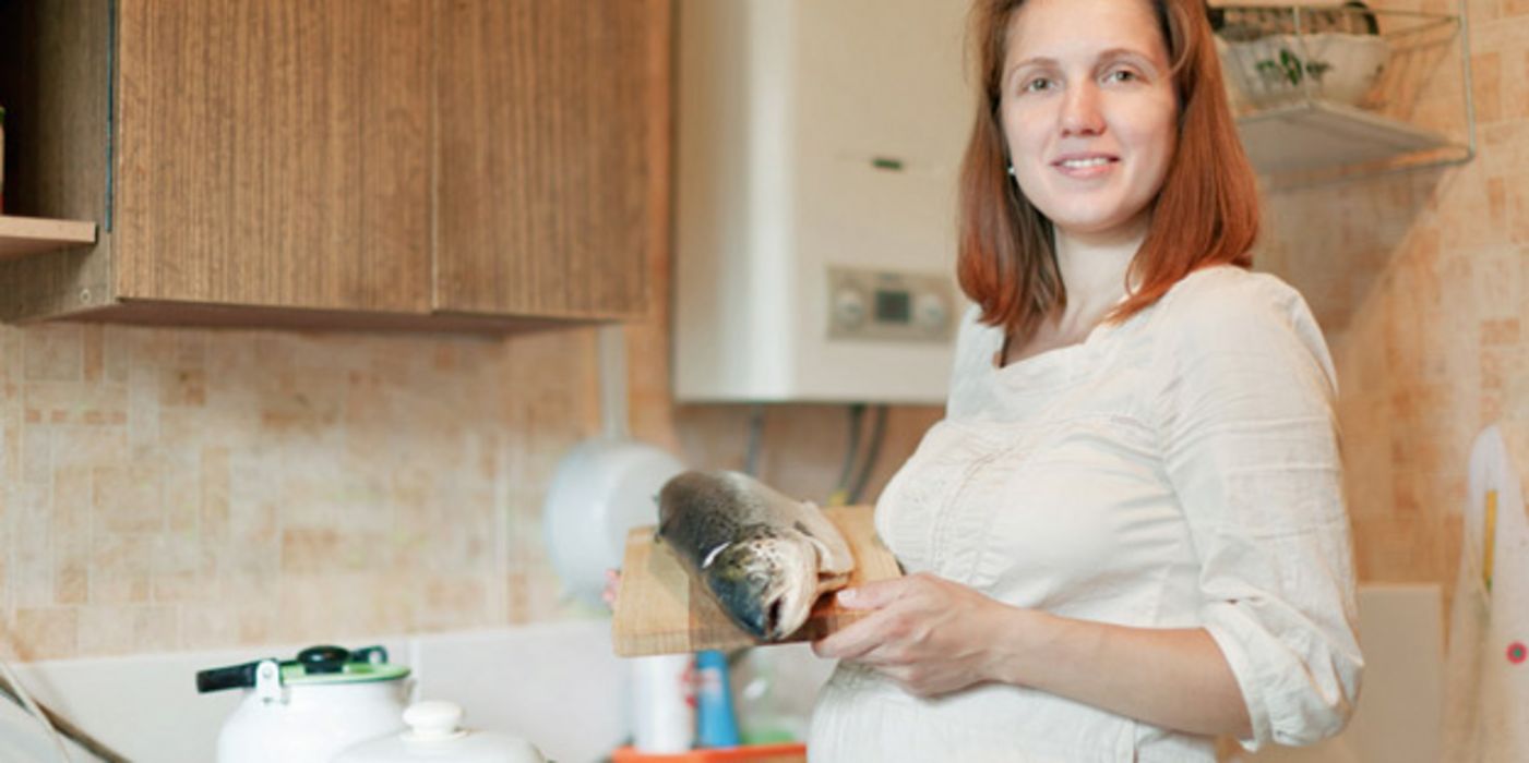 Schwangere steht mit einem Lachs in der Küche