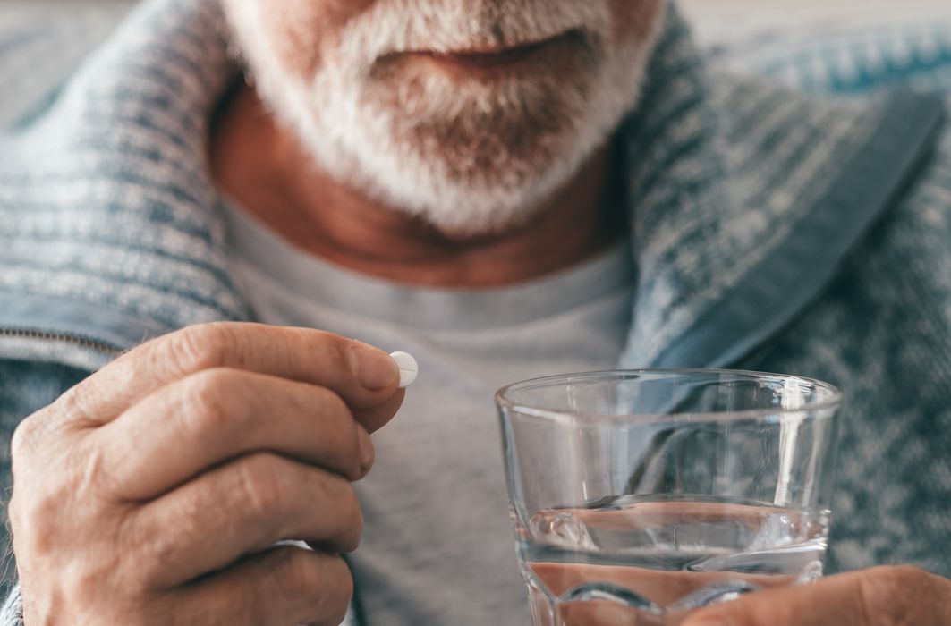 Älterer Mann, nimmt eine Tablette mit einem Glas Wasser.