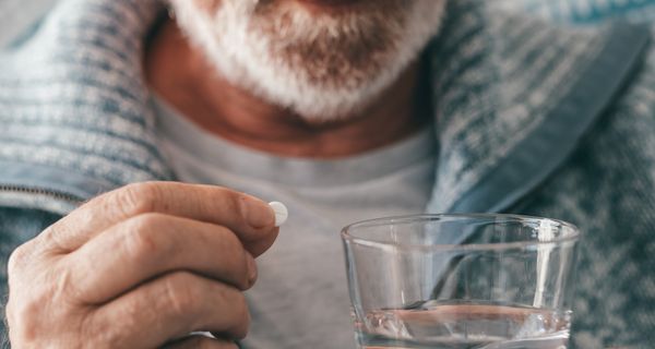 Älterer Mann, nimmt eine Tablette mit einem Glas Wasser.