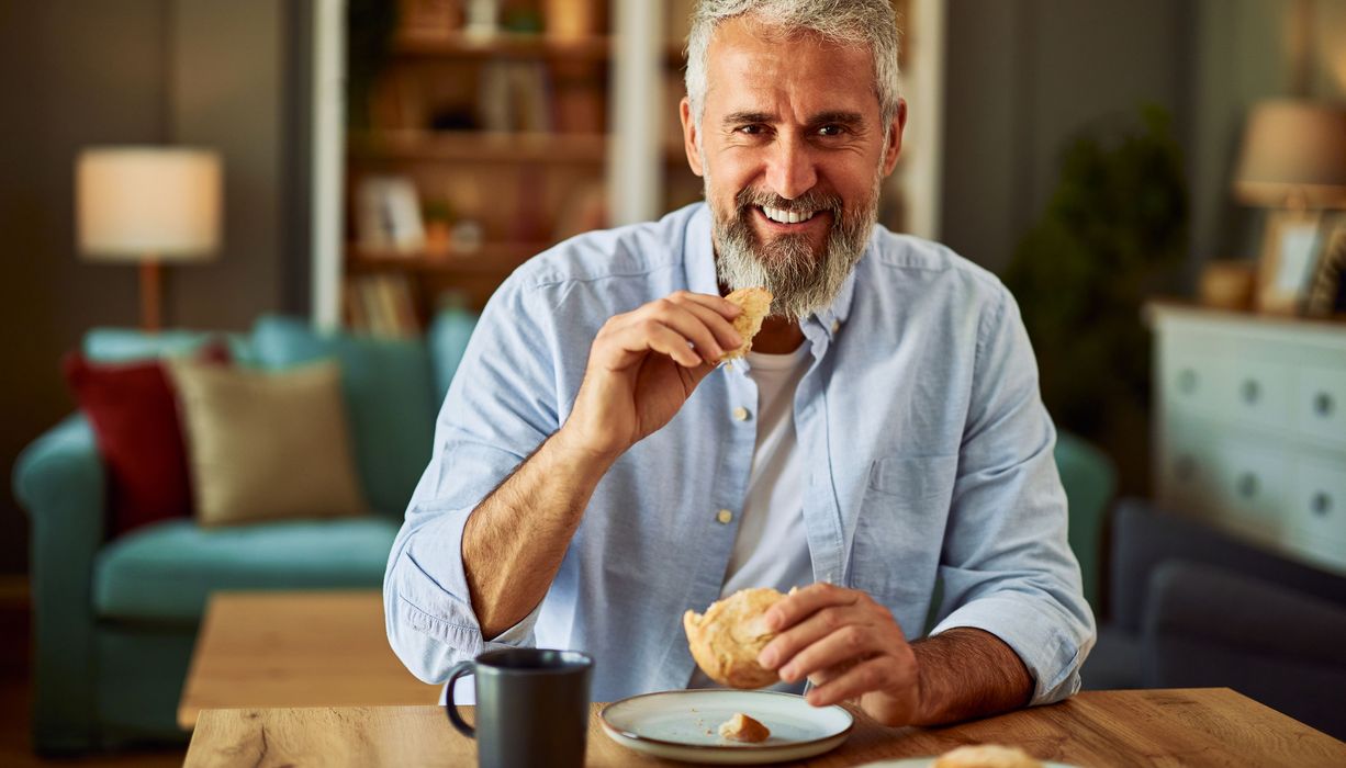 Mann 40+ isst ein Brötchen.