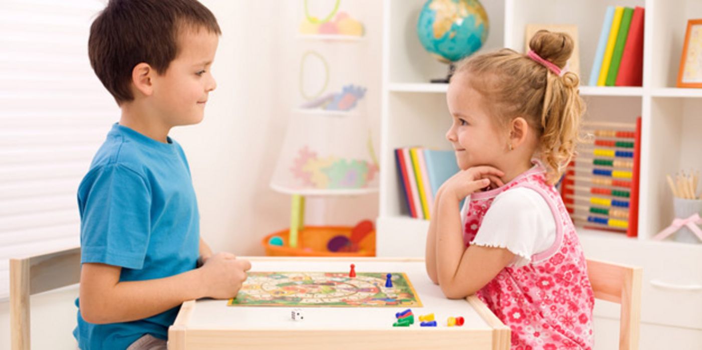 Mädchen und Junge sitzen am Tisch und spielen ein Brettspiel.