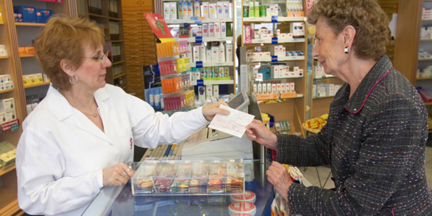 Apothekerin nimmt Rezept von älterer Kundin entgegen.