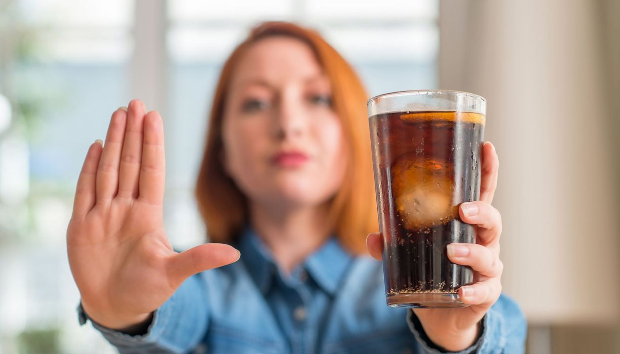 Frau, hält ihre Hand und ein Glas Cola in die Kamera.