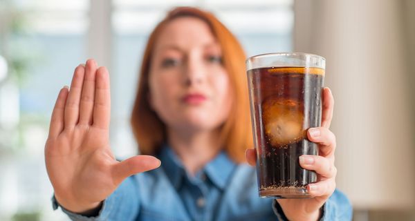 Frau, hält ihre Hand und ein Glas Cola in die Kamera.