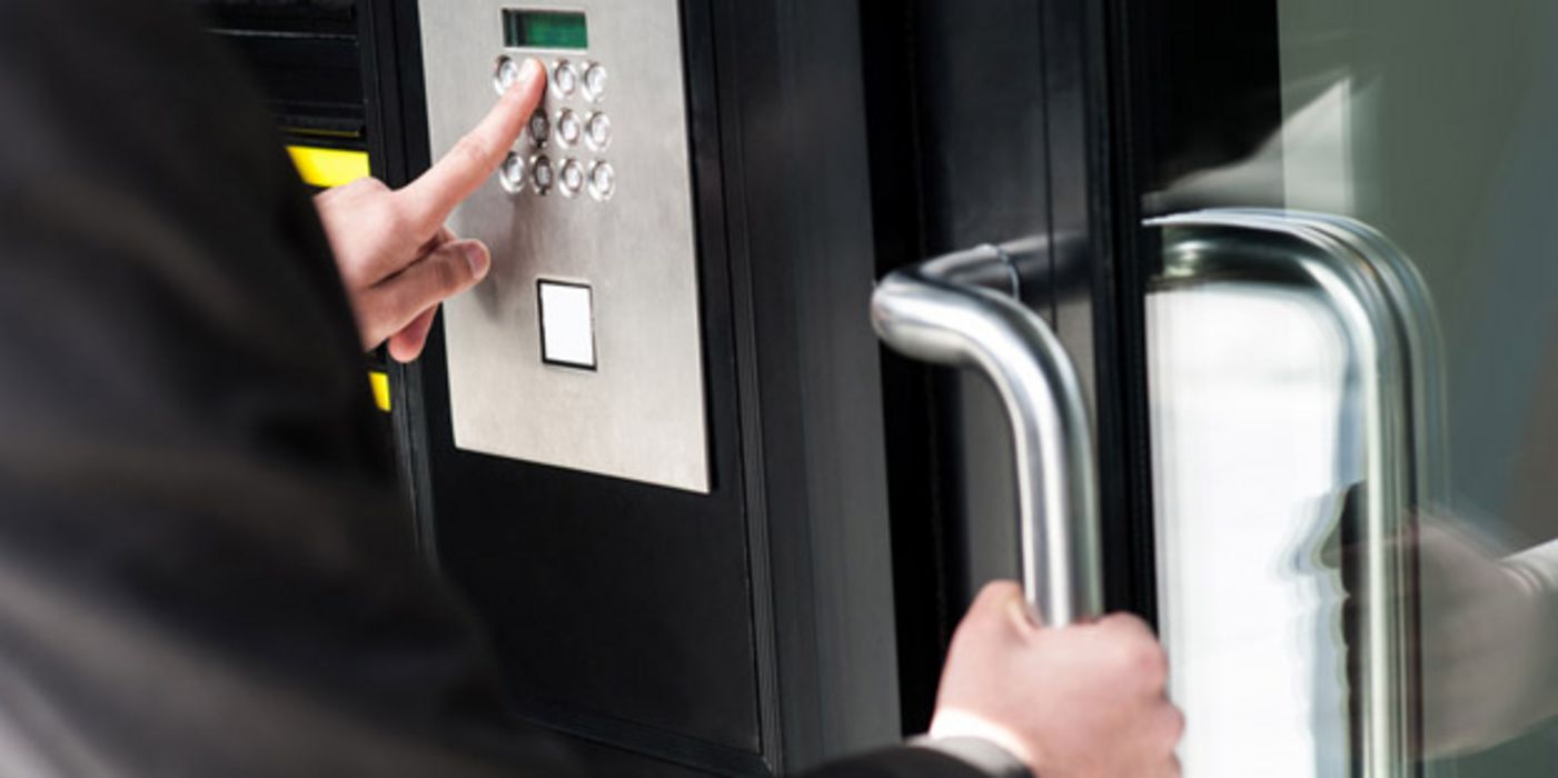 Mann im Anzug mit einer Hand am Türgriff und der anderen Hand auf einer Nummernpad