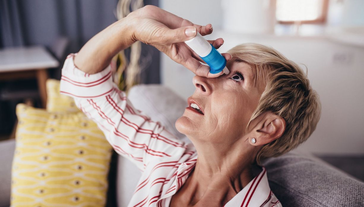 Frau, tropft sich Augentropfen in das Auge.