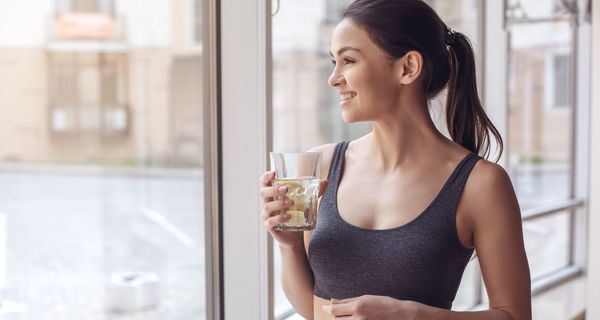 Sportlich gekleidete Frau trinkt ein Glas Leitungswasser.