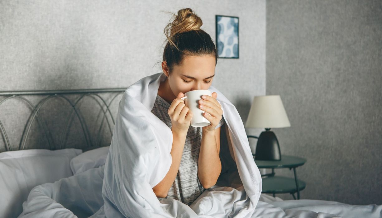 Junge Frau, sitzt im Bett und trinkt Kaffee.