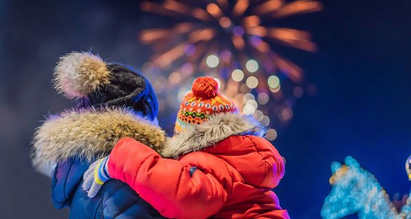 Rückansicht von Vater und Kind, die in dicken Winterjacken ein Feuerwerk in der Ferne betrachten.