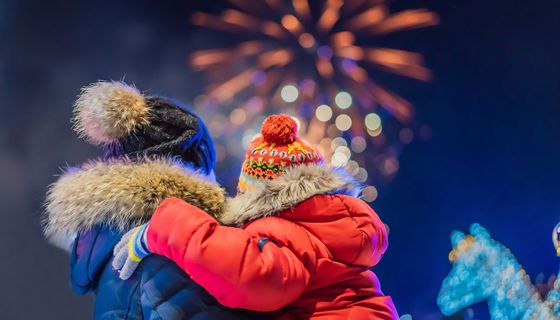 Rückansicht von Vater und Kind, die in dicken Winterjacken ein Feuerwerk in der Ferne betrachten.