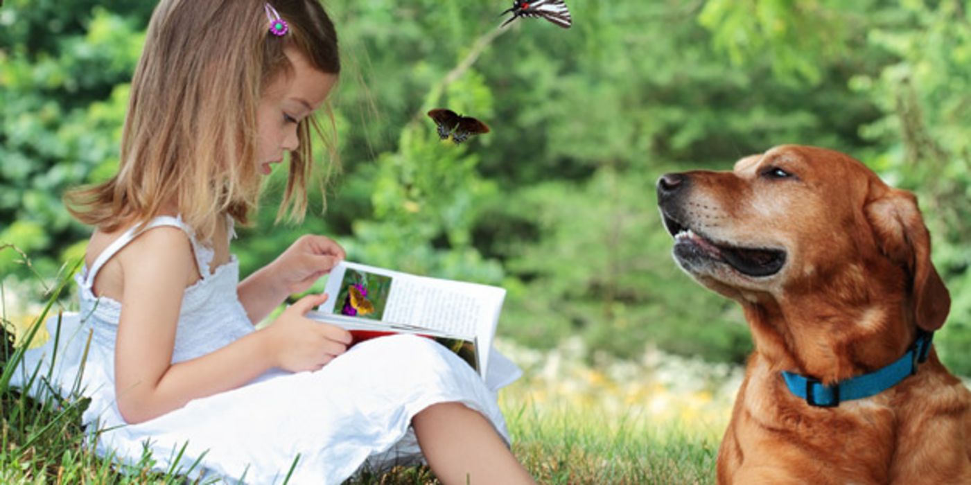 Mädchen liest einem Hund ein Buch vor