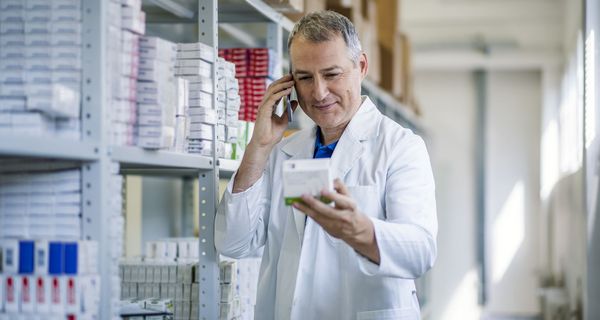 Apotheker, hält ein Medikament in der Hand und telefoniert.