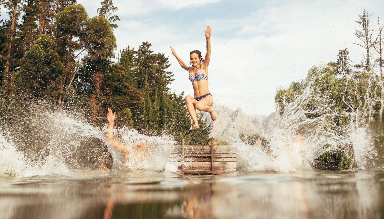 Junge Frauen, springen von einem Steg in einen See.