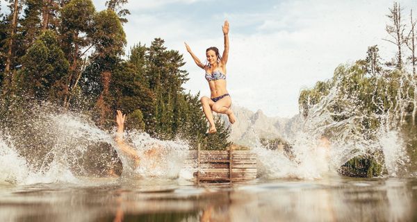 Junge Frauen, springen von einem Steg in einen See.