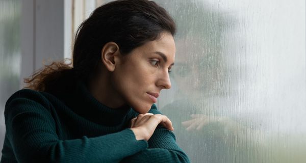 Frau, schaut traurig zur Seite aus dem Fenster.