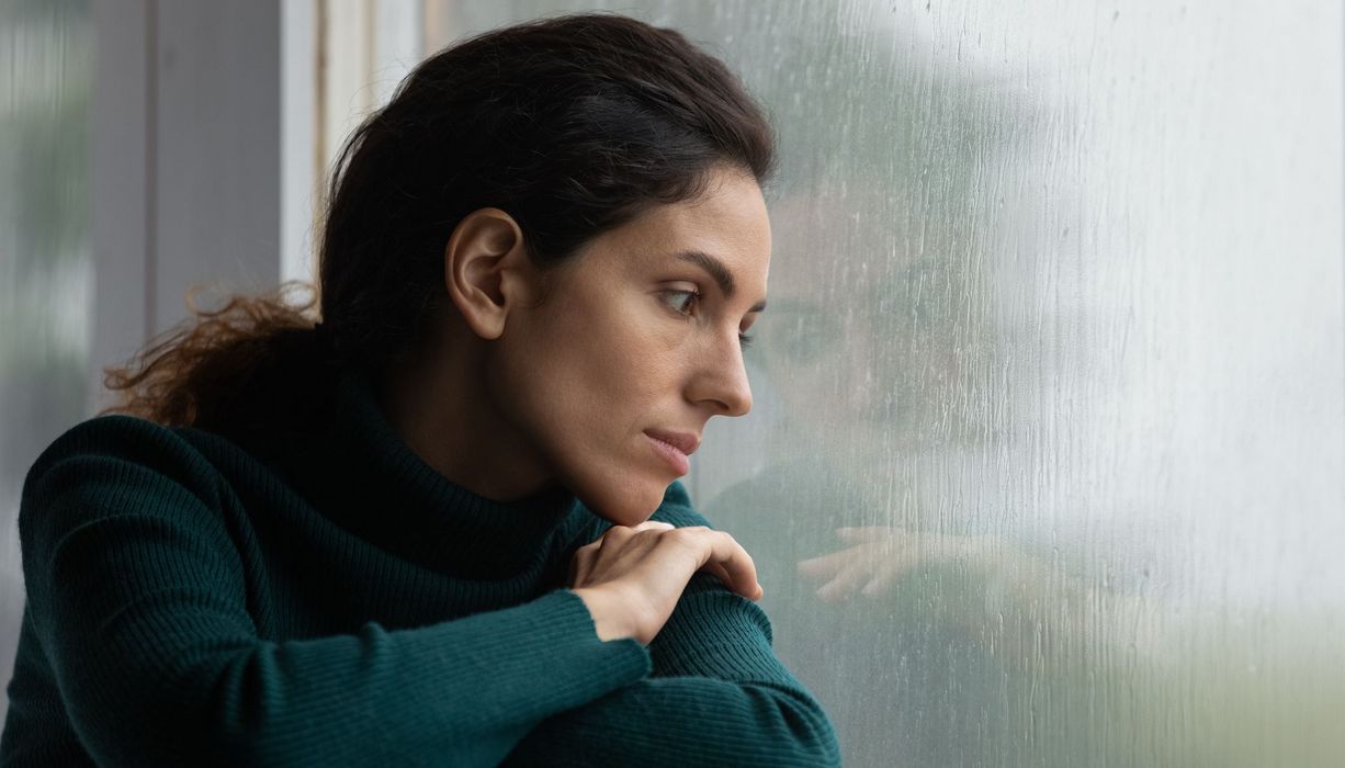 Frau, schaut traurig zur Seite aus dem Fenster.