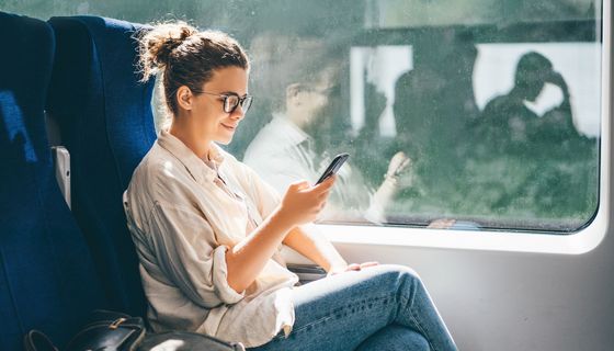 Frau, sitzt im Zug und schaut auf ihr Handy.