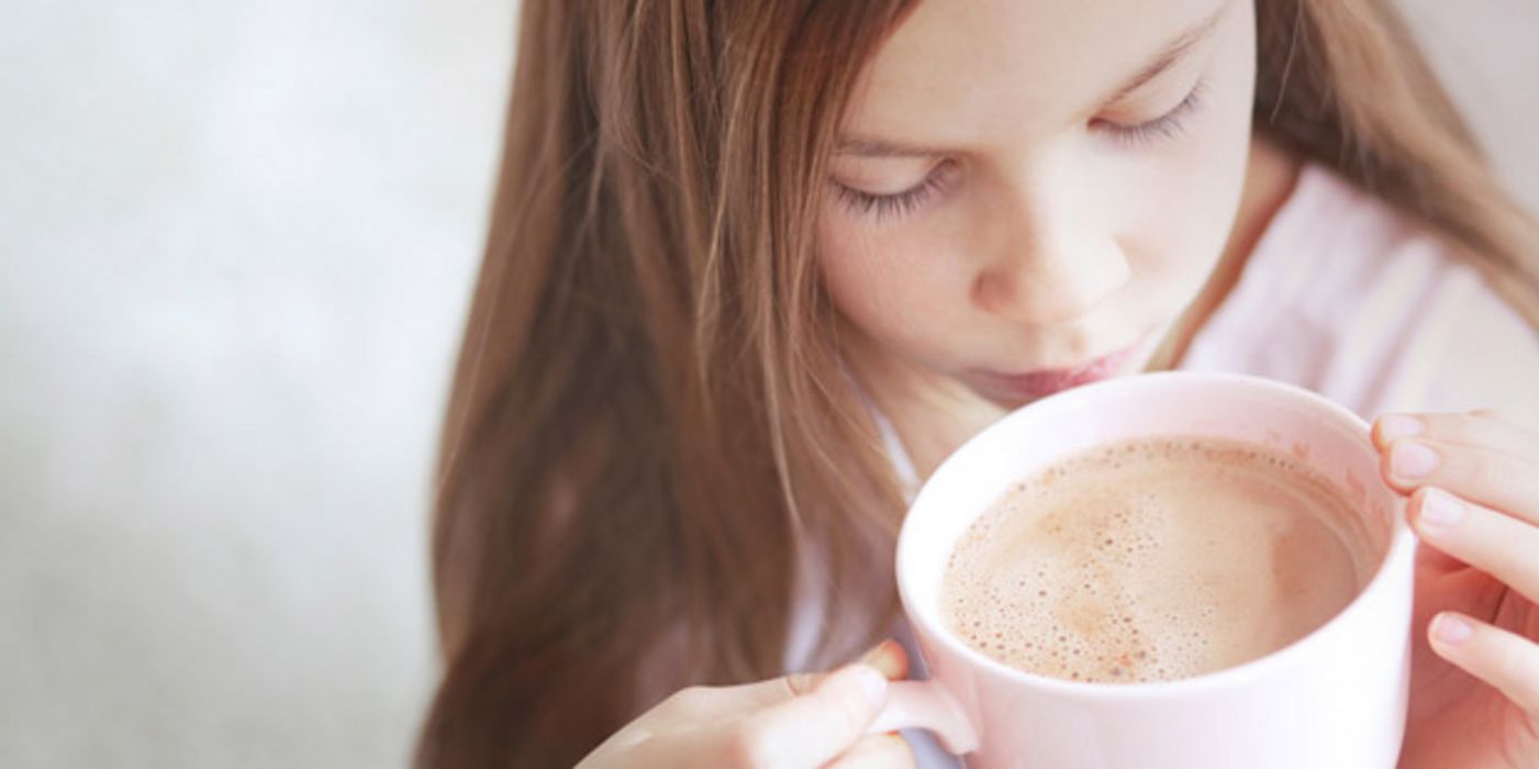 7-jähriges Mädchen von schräg oben fotografiert, trinkt aus einer Tasse Kakao.