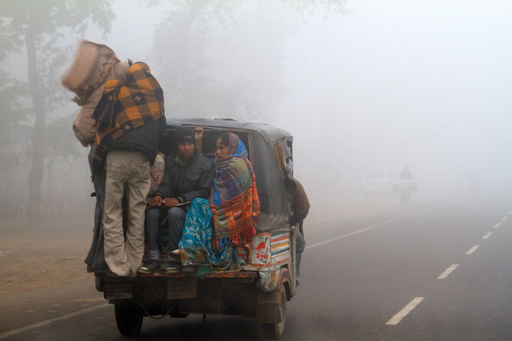 Eine indische Familie wird bei extrem rauen Wetterbedingungen in einer Auto-Rikscha transportiert. Neu-Delhi, eine landumschlossene, schnell wachsende Metropole mit mehr als 16 Millionen Einwohnern, ist in den Wintermonaten regelmäßig von Dunst und Smog (manchmal euphemistisch als Nebel bezeichnet) umhüllt, da sich Luftdruck und kühlere Luft mit Baustaub, Rauch von Kuhmistbränden und Autoabgasen vermischen, die dann tagelang über der Stadt schweben.