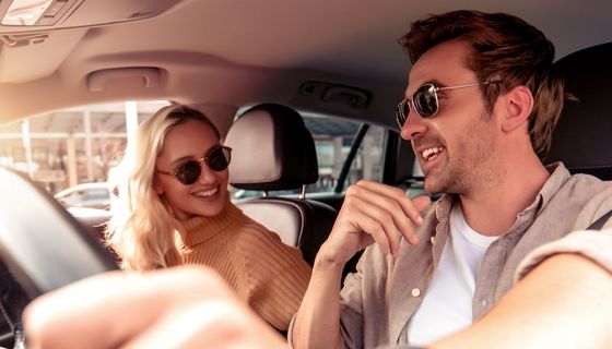 Paar unterhält sich beim Autofahren: Der Mann gestikuliert am Steuer, die Frau hat sich ihm zugewandt.