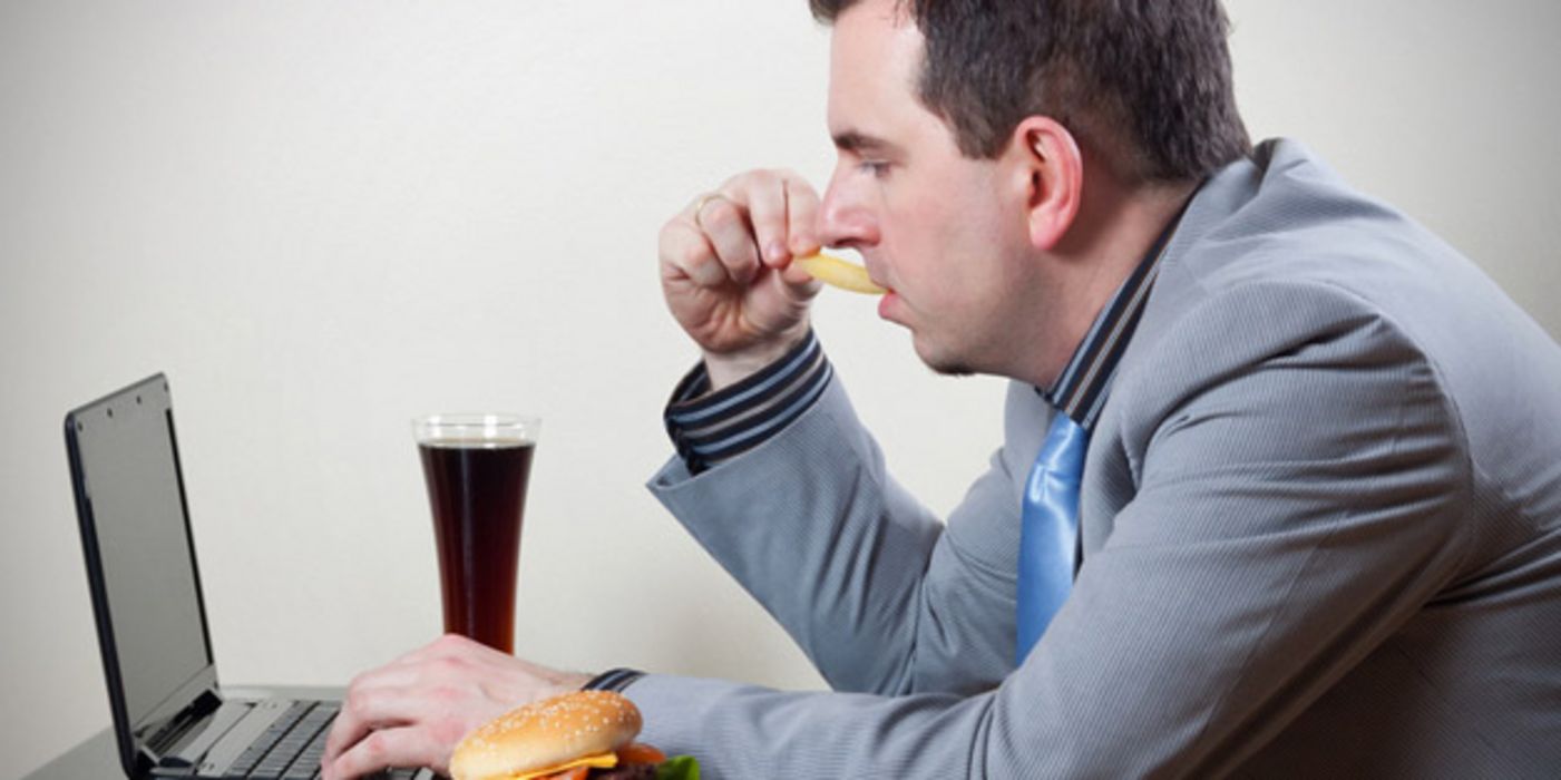 Mann sitzt vor einem Laptop und isst Fastfood