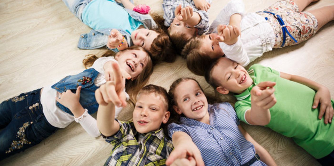 Sieben fröhliche Kinder liegen sternförmig auf dem Boden.