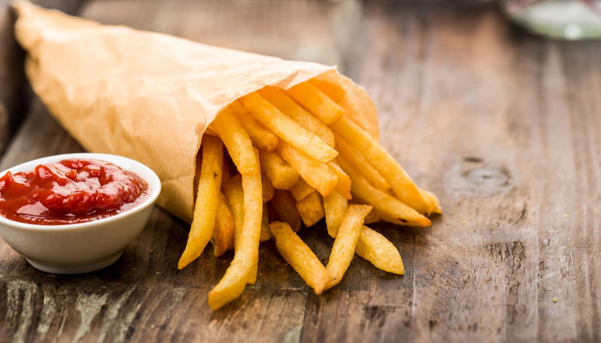 Pommes in einer Tüte, daneben eine Portion Ketchup.