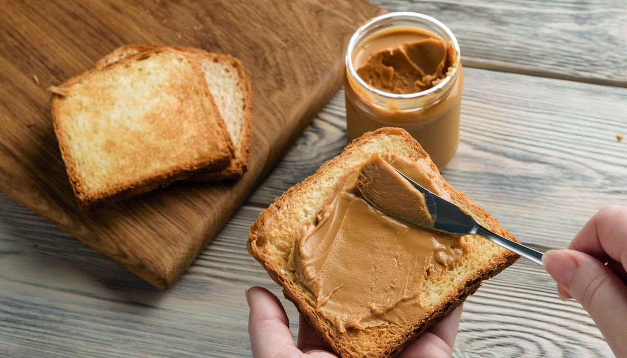 Frau, schmiert Erdnussbutter auf eine Scheibe Toast.