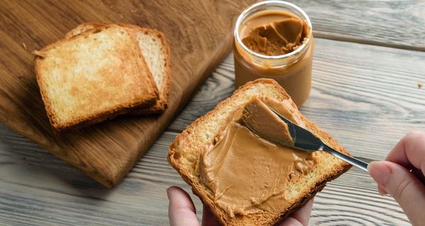 Frau, schmiert Erdnussbutter auf eine Scheibe Toast.