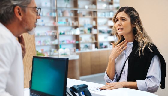 Frau mit Halsschmerzen, spricht mit einem Apotheker.