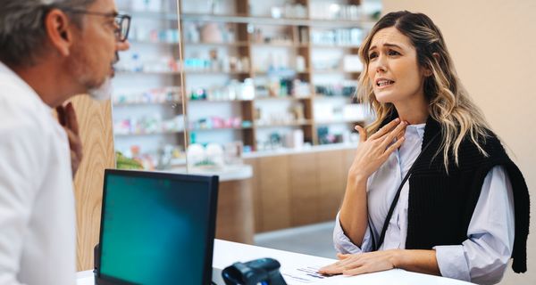 Frau mit Halsschmerzen, spricht mit einem Apotheker.