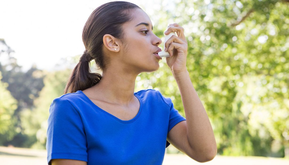 Junge Frau, draußen im Freien, nutzt Asthmaspray.