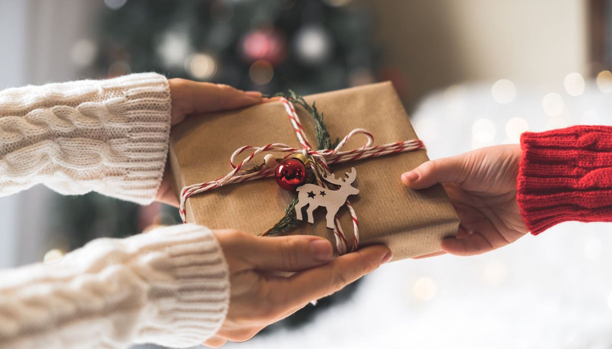 Hände, die ein festliches Geschenk übergeben.