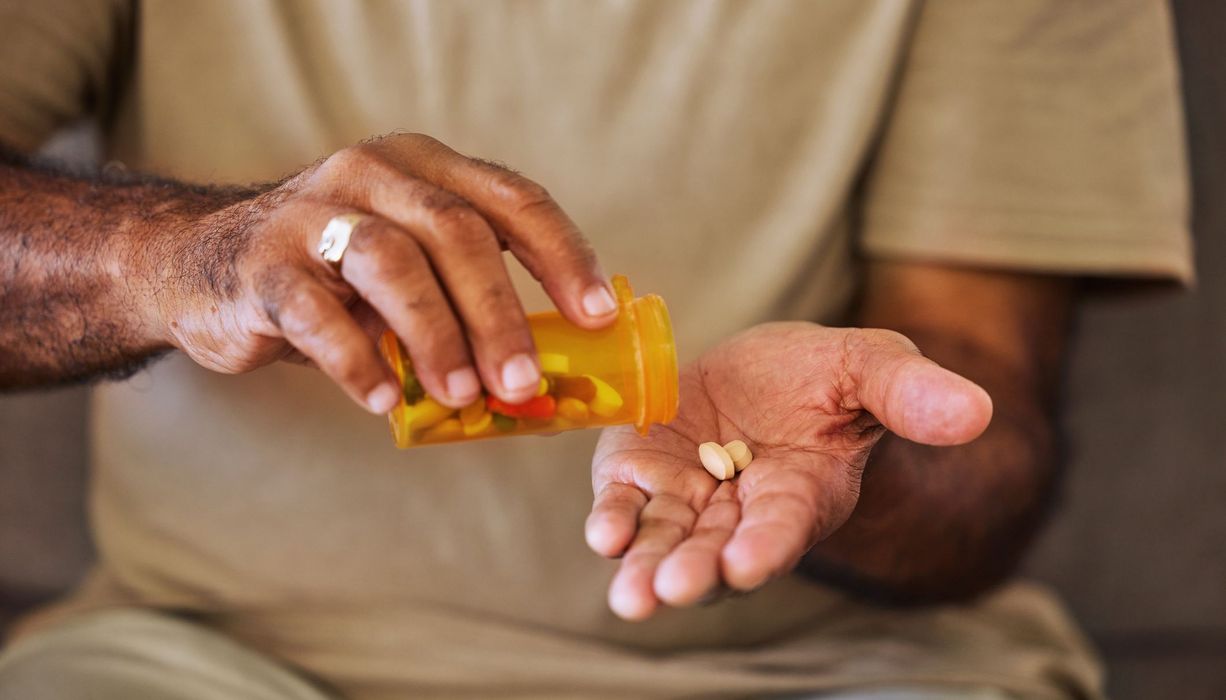 Mann, schüttet sich aus einer Dose Tabletten in eine Hand.