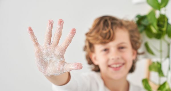 Kind, streckt eine eingeseifte Hand in die Kamera.