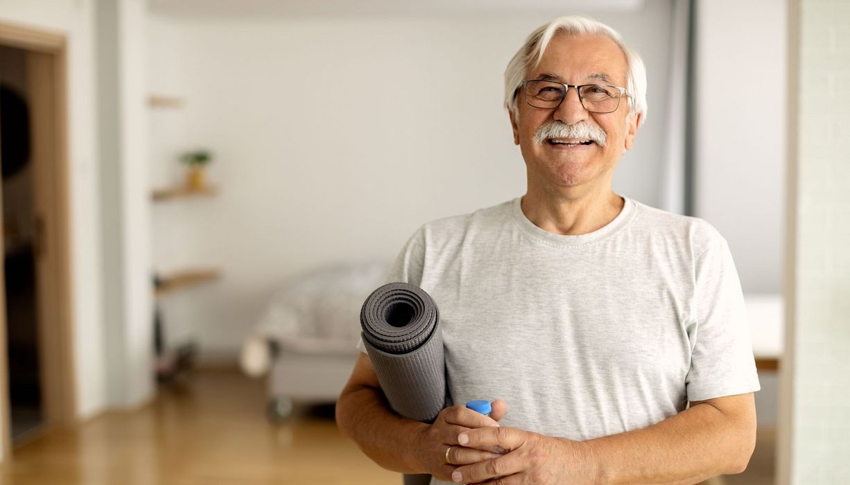 Sportlicher älterer Mann mit Yoga-Matte unter dem Arm.