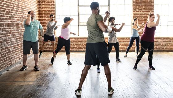 Ein Mann leitet eine Gruppe von Frauen und Männern verschiedenen Alters bei Sportbewegungen an.