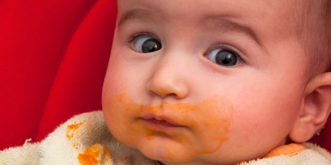 Nahaufnahme eines breiverschmierten Kleinkindergesichts mit erstaunt aufgerissenen Augen