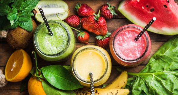 Drei Fruchtsäfte mit Obst daneben.