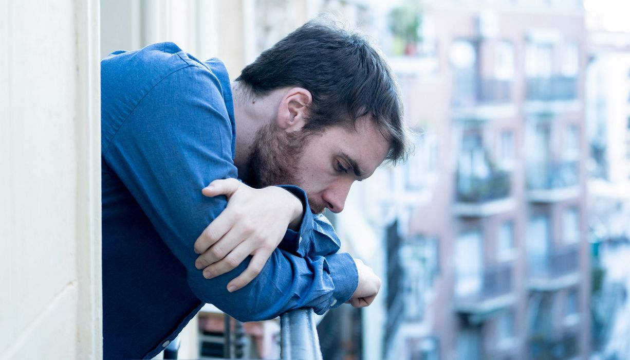 Mann steht am Balkon und schaut deprimiert nach unten