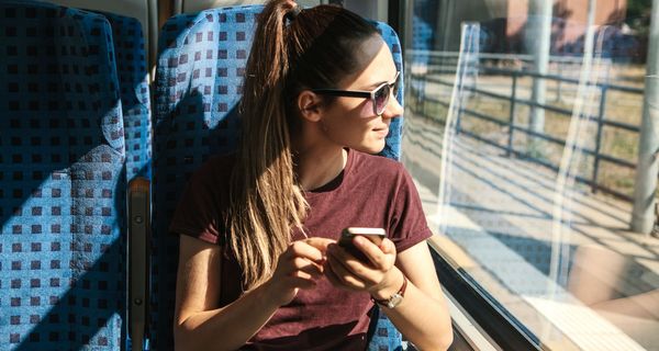 Junge Frau, sitzt in der Bahn, Sonne scheint durch das Fenster.