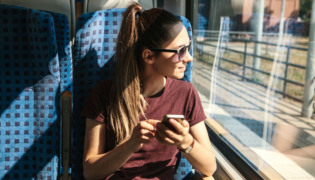 Junge Frau, sitzt in der Bahn, Sonne scheint durch das Fenster.