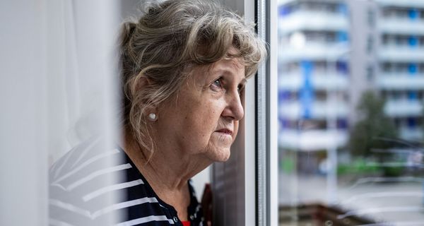 Ältere Frau, schaut nachdenklich aus dem Fenster.