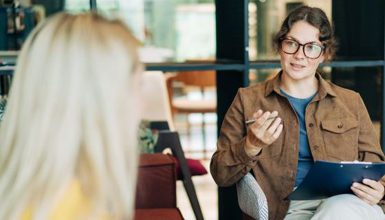 Eine Psychotherapeutin im Gespräch mit einer Patientin. Letztere ist nur von hinten zu sehen.