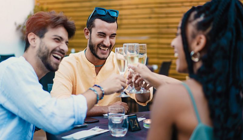 Junge, gutgelaunte Menschen stoßen mit einem Glas Sekt an.