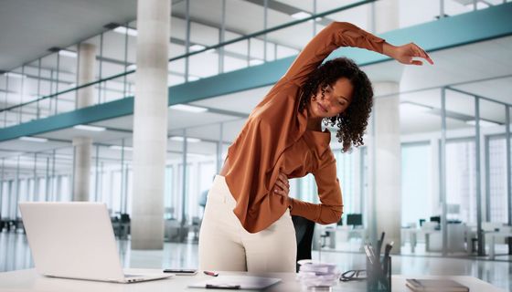 Eine Frau ist vom Laptop aufgestanden und streckt sich.