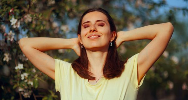 Frau hält Gesicht und Arme der Sonne entgegen. 